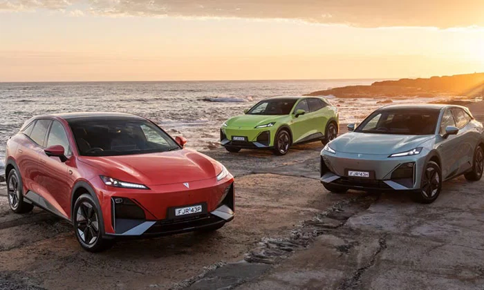 Three Deepal S07 electric SUVs in red, green, and blue parked on a rocky Australian coastline at sunset
