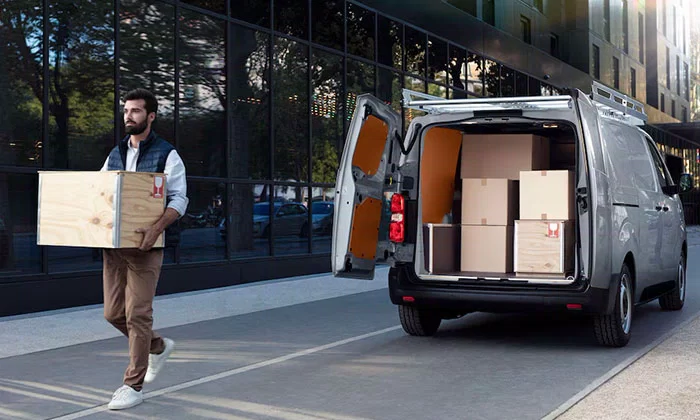 Peugeot Expert van rear view with back doors fully open, cargo area filled with boxes, and a man carrying a box walking away on a delivery